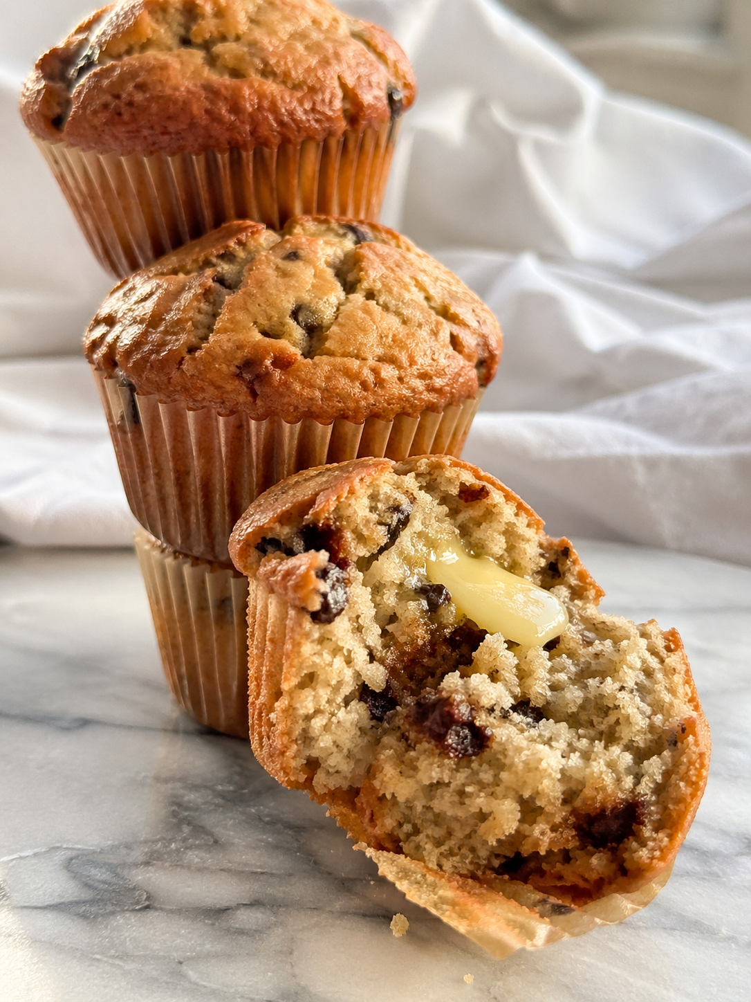 Banana muffins stacked on marble surface, one split open showing fluffy interior