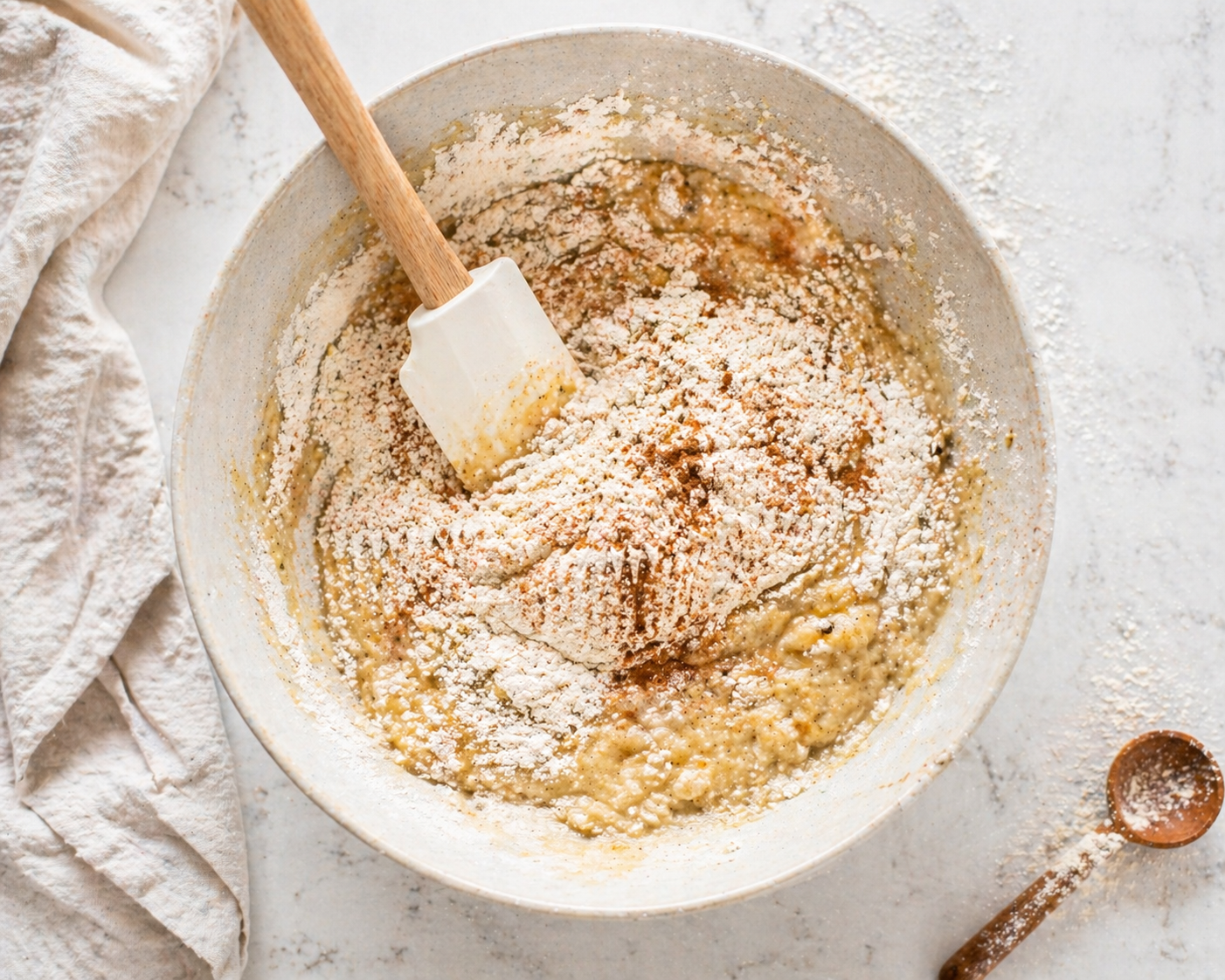 Folding dry ingredients into banana muffin batter in a mixing bowl