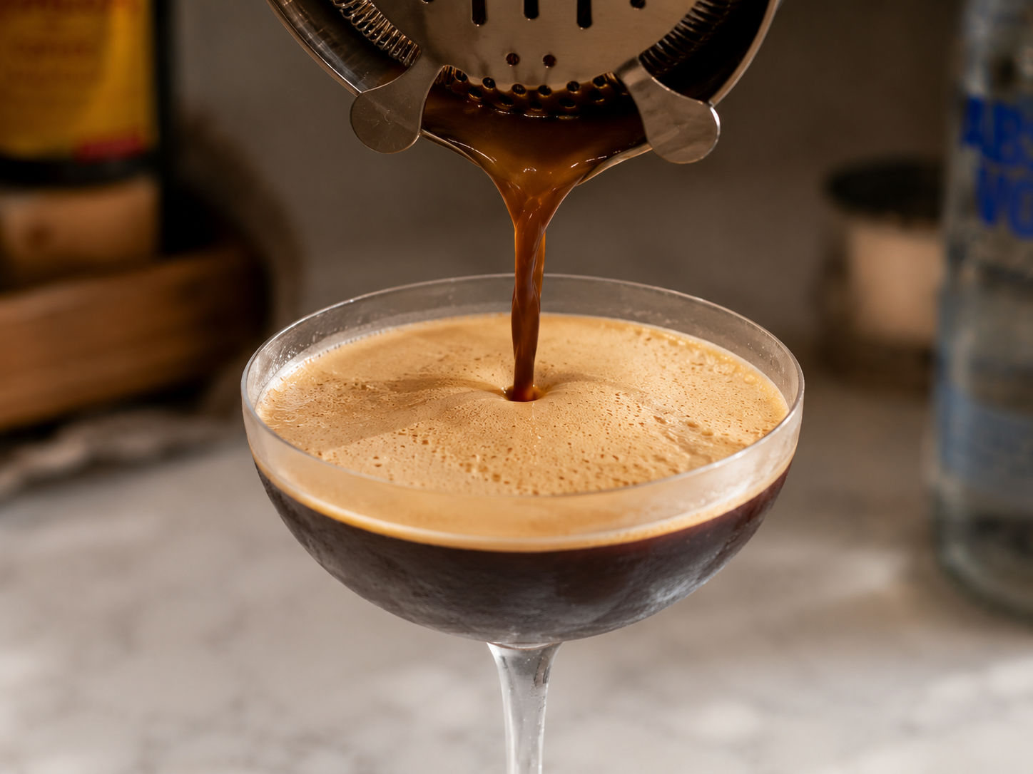 Espresso martini being strained into a chilled martini glass — foam rising beautifully to the top