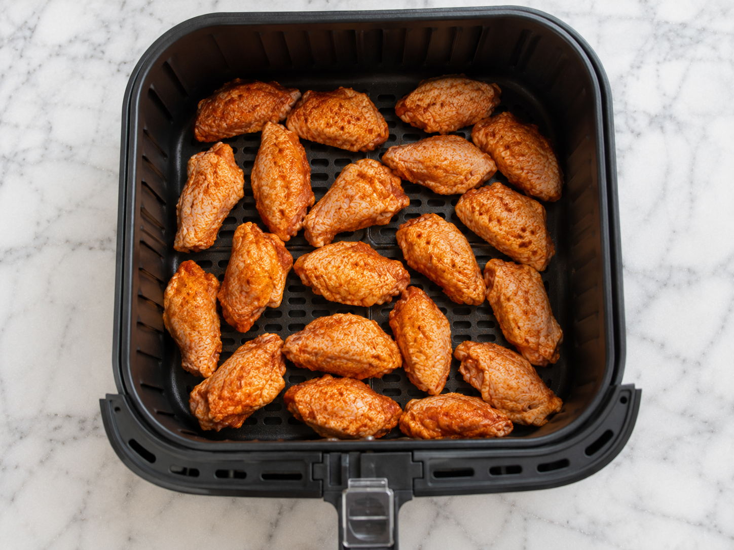 Seasoned wings arranged in a single layer in the air fryer basket with space between each piece