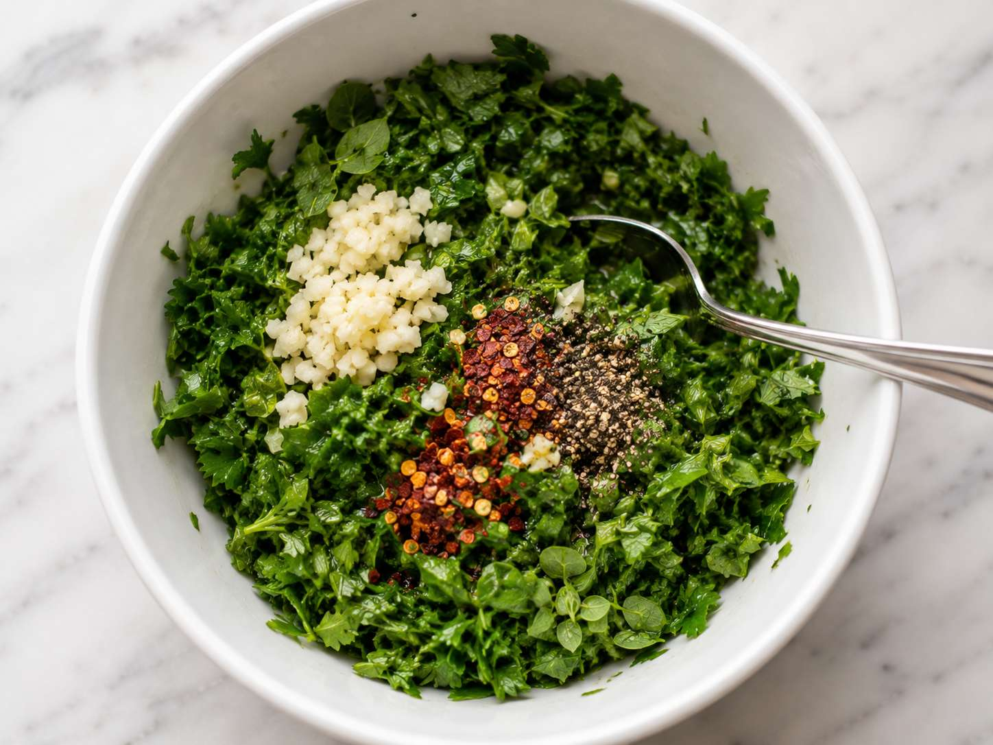 Minced garlic, red pepper flakes, salt and pepper added to the chopped herbs in a bowl