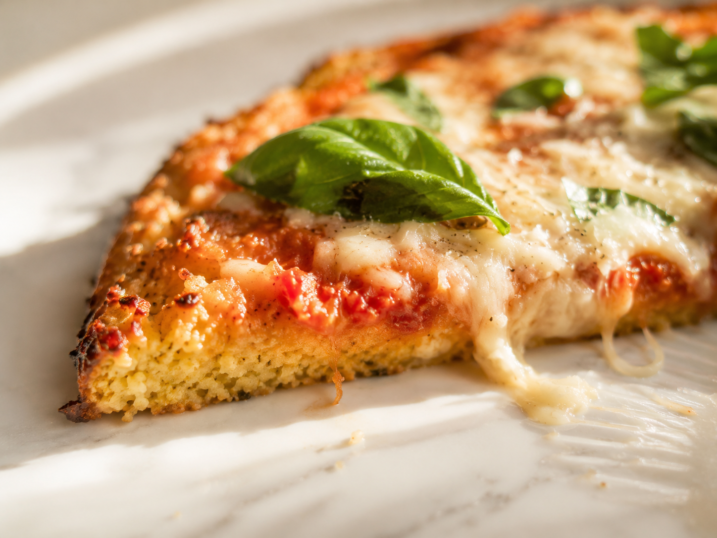 Finished cauliflower pizza sliced and ready to serve — crispy edges, melted cheese and fresh basil