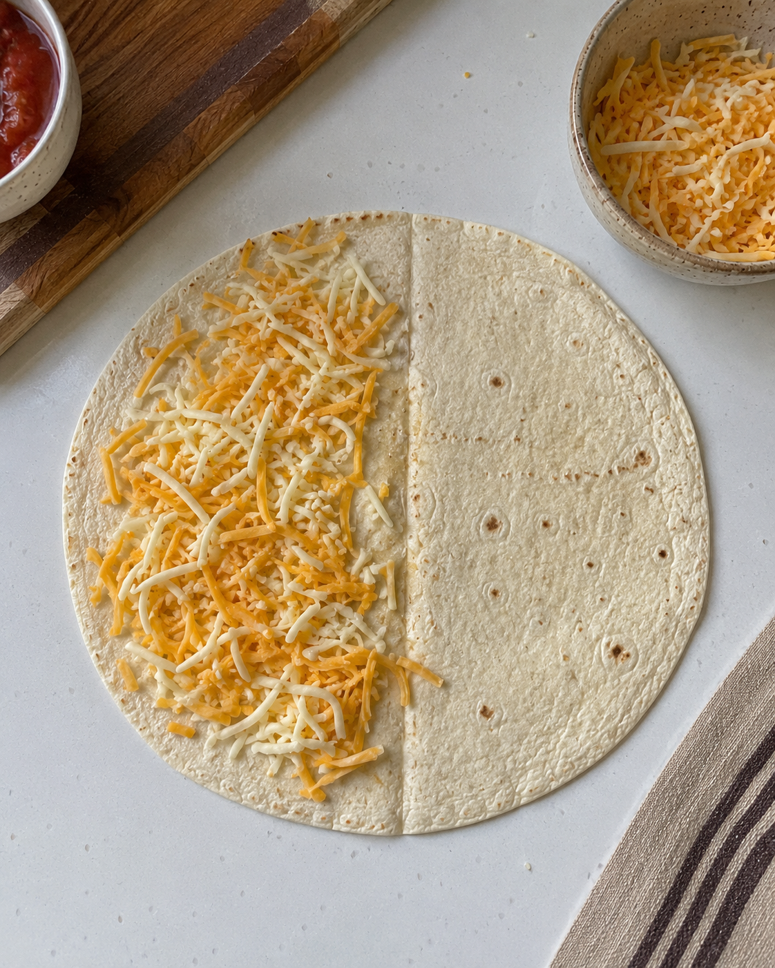 Flour tortilla laid flat with shredded cheese on one half and beef filling added on top