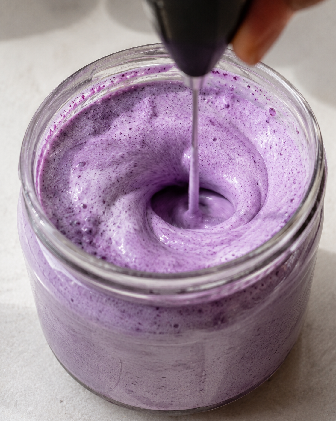 Handheld frother whipping blueberry cream into a thick, fluffy purple cloud foam