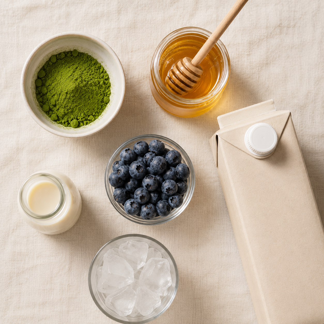All blueberry cloud matcha ingredients laid out: matcha powder, blueberries, oat milk, honey, heavy cream and ice