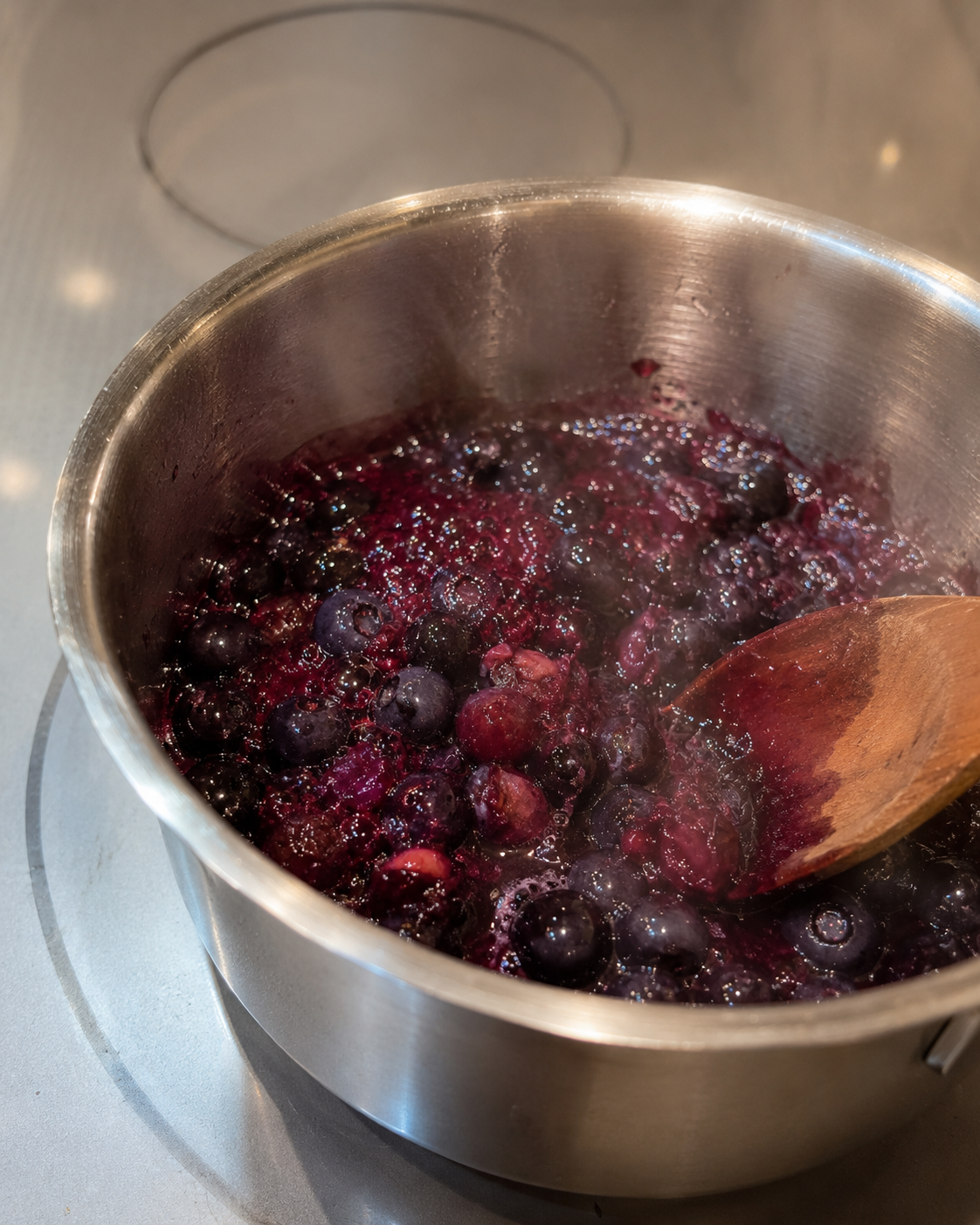 Blueberries simmering in a small saucepan, bursting and releasing deep purple juice