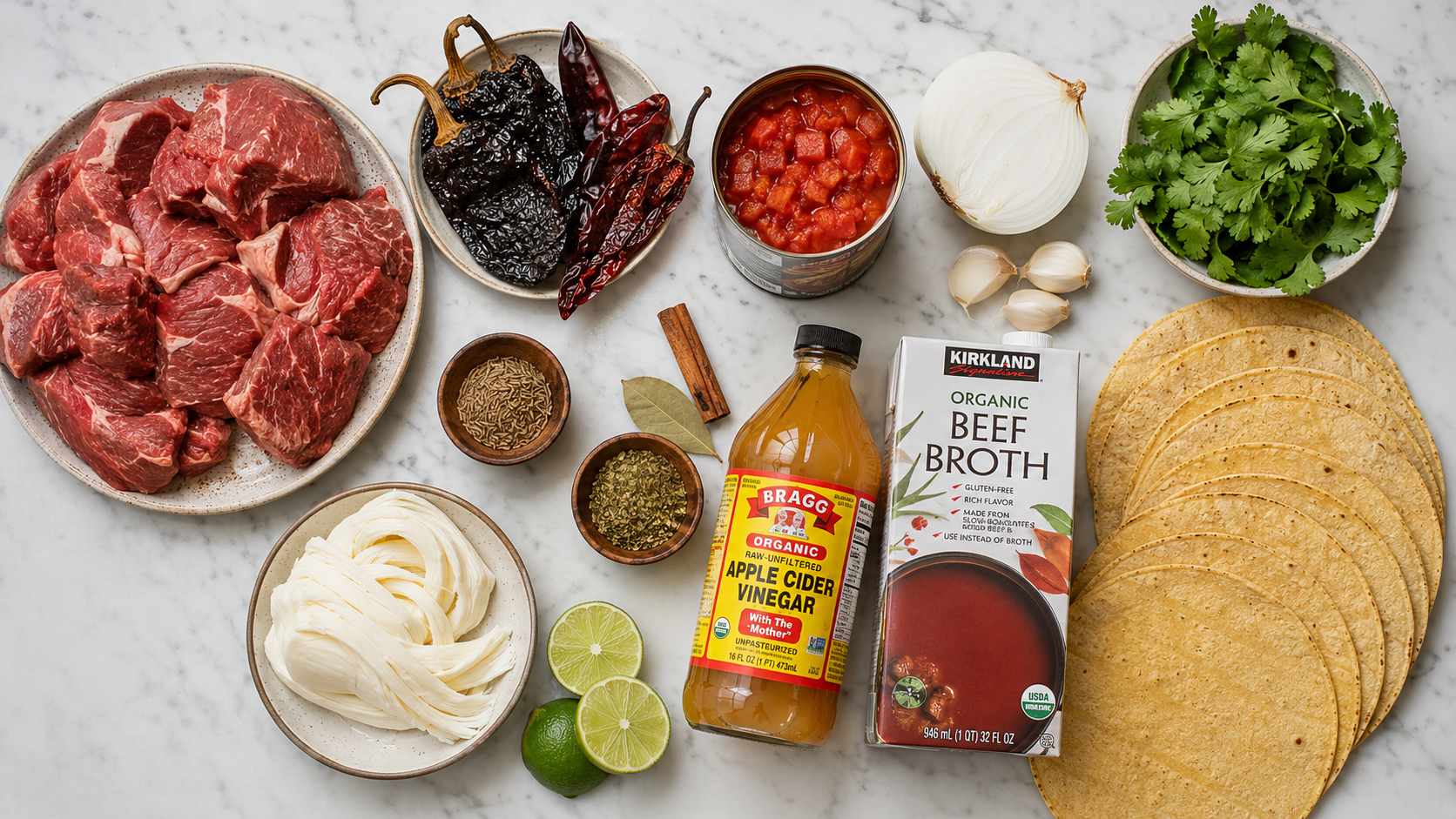 All birria taco ingredients laid out &mdash; dried chiles, beef chuck, spices, tomatoes, onion, tortillas and cheese