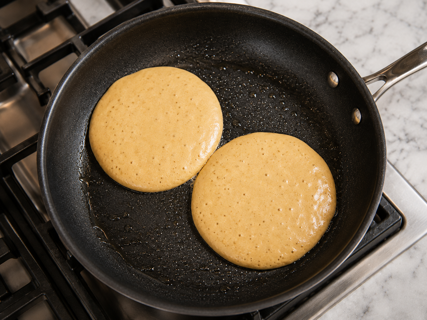 Protein pancakes cooking in the skillet — bubbles forming on the surface, edges just setting