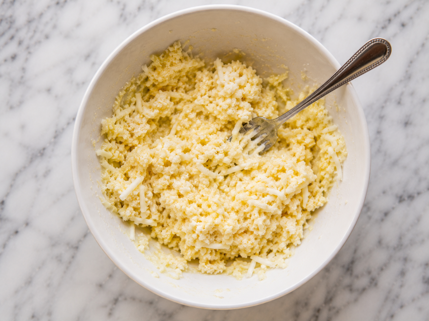 Squeezed cauliflower mixed with egg, mozzarella, parmesan and seasonings in a bowl — soft dough formed