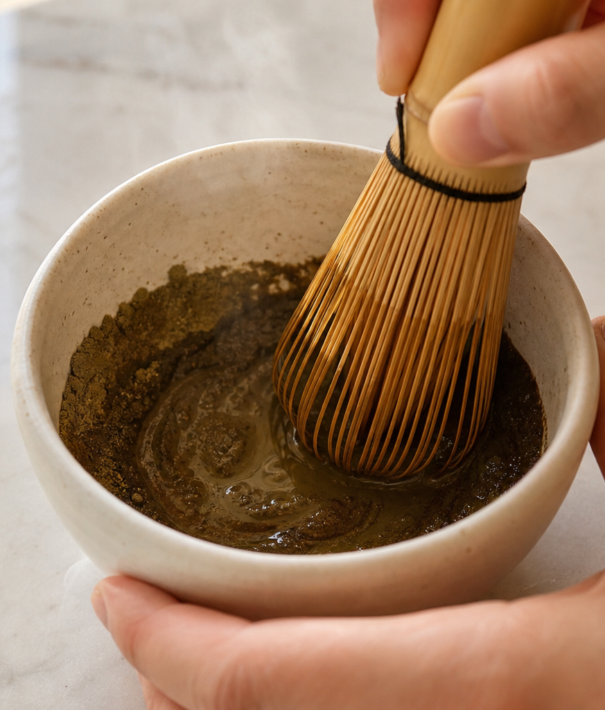 Hojicha powder being whisked with a small amount of hot water into a smooth paste in a ceramic bowl