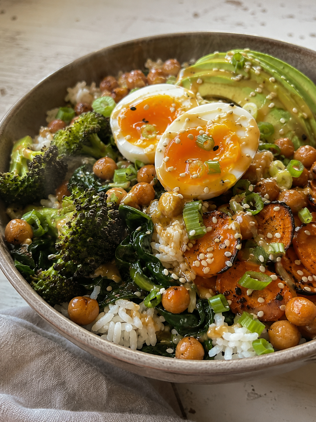 Miso-ginger umami bowl with roasted broccoli, caramelized carrots, crispy chickpeas, soft-boiled egg and avocado over rice