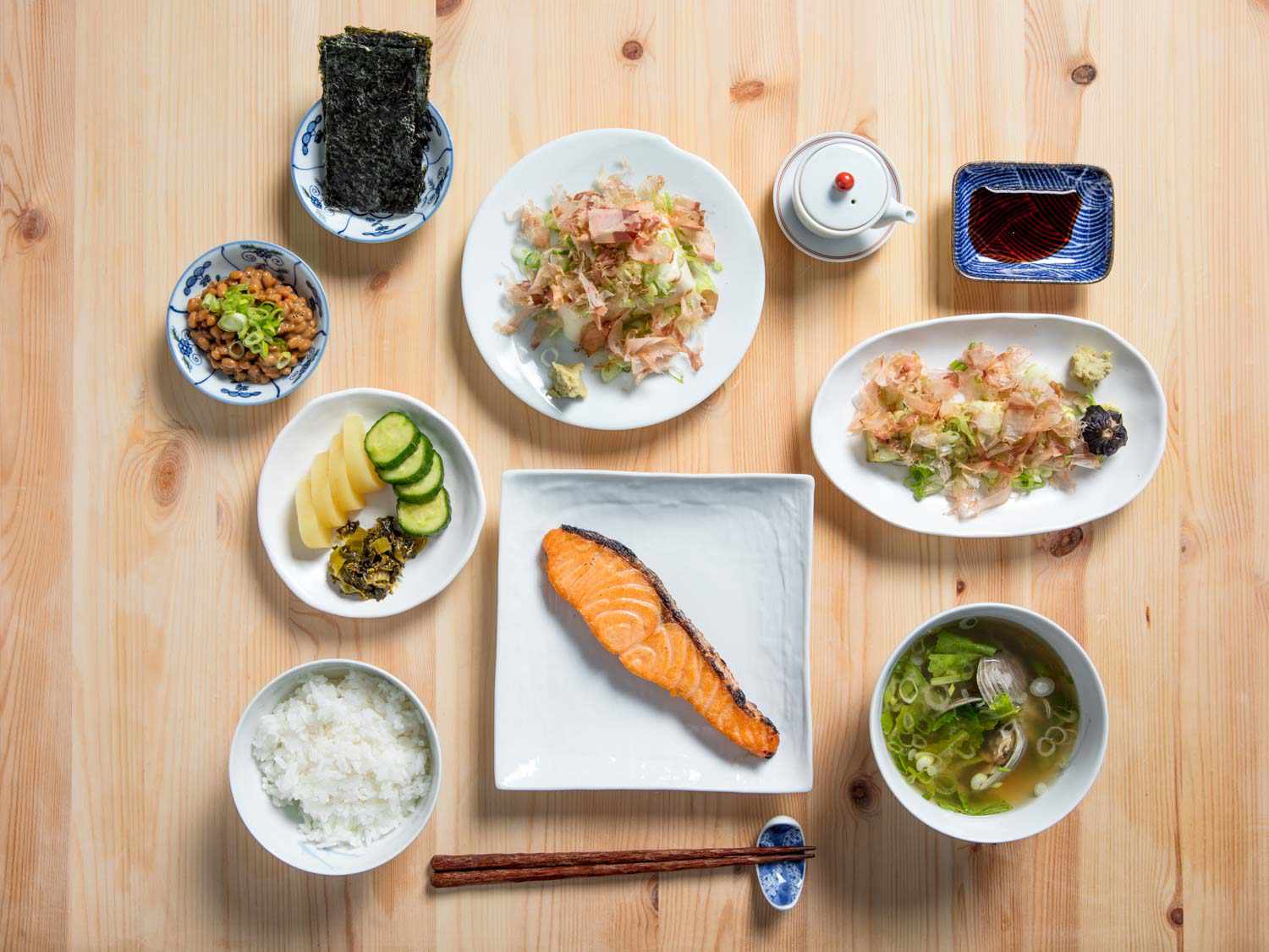 Traditional Japanese breakfast spread — miso soup, rice, pickled vegetables, grilled fish in ceramic bowls