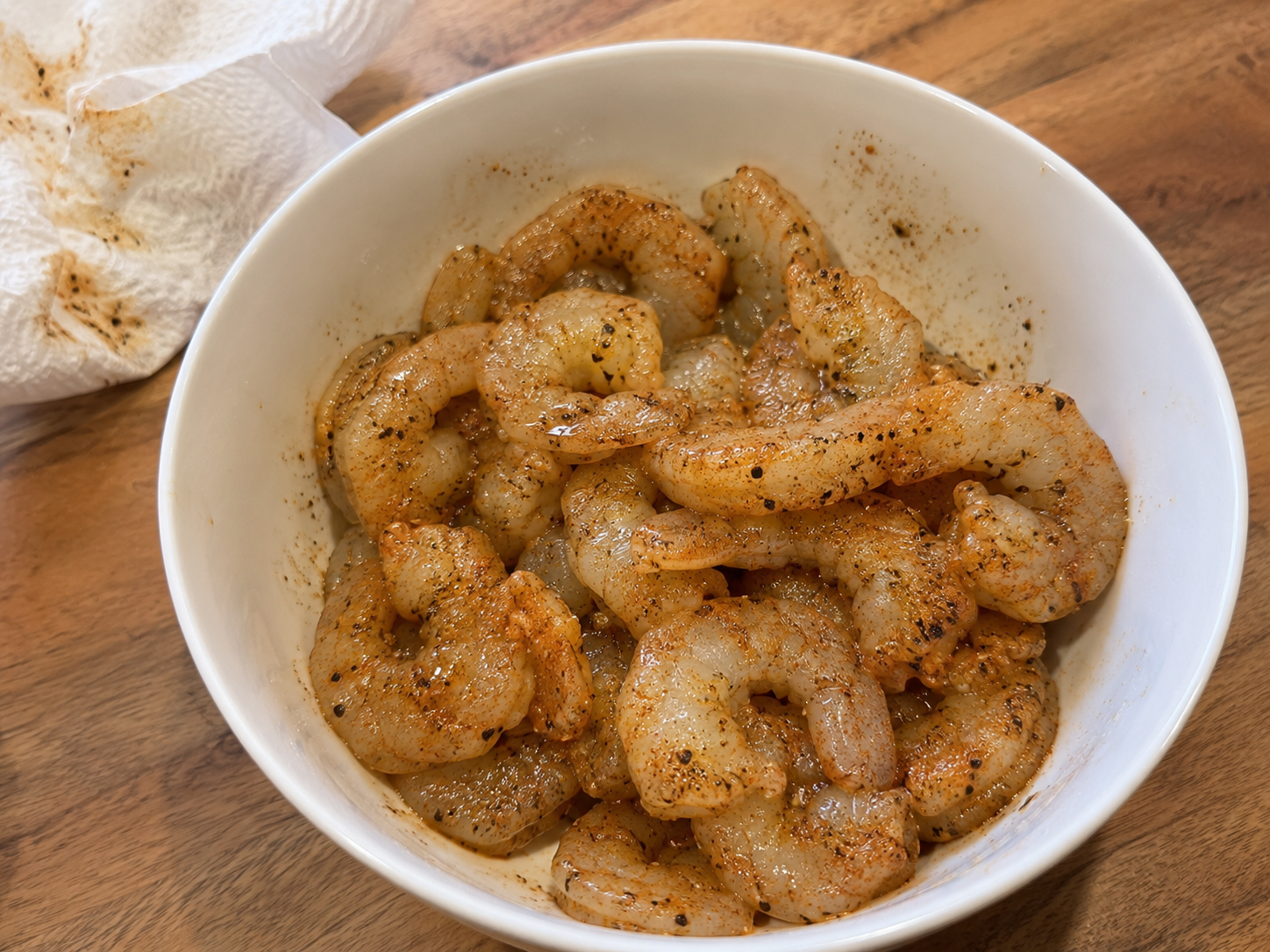 Raw shrimp seasoned with garlic powder, paprika, salt and pepper in a bowl — ready to sear