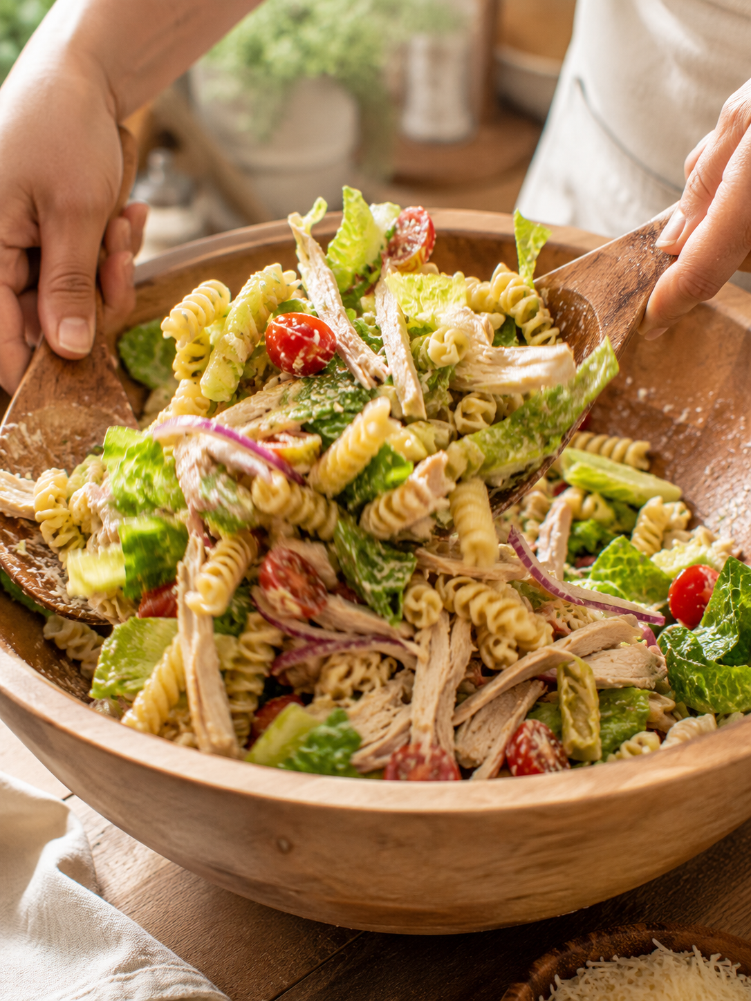 Pasta, chicken, tomatoes and romaine being tossed with Caesar dressing in a large bowl