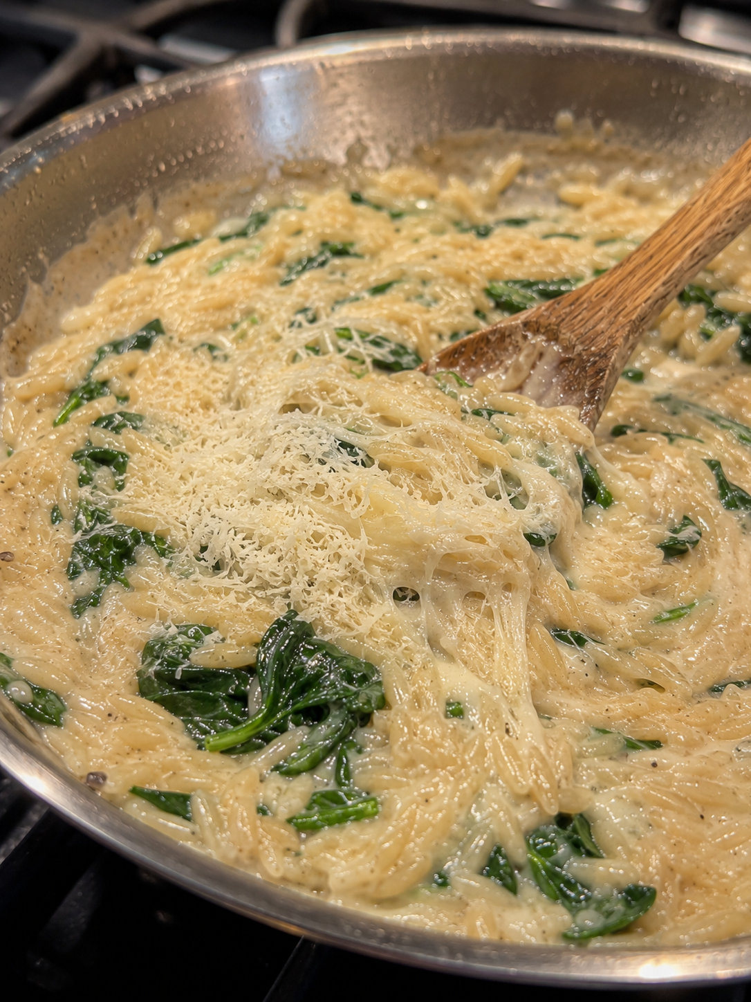 Grated parmesan melting into the creamy orzo — sauce turning silky and glossy