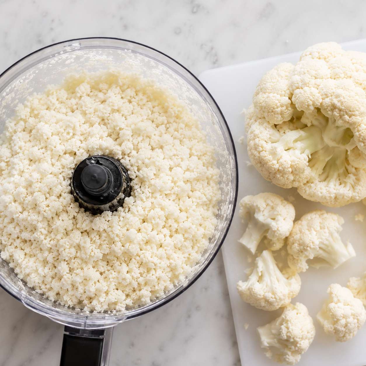 Cauliflower florets being pulsed in a food processor into fine rice-like crumbs