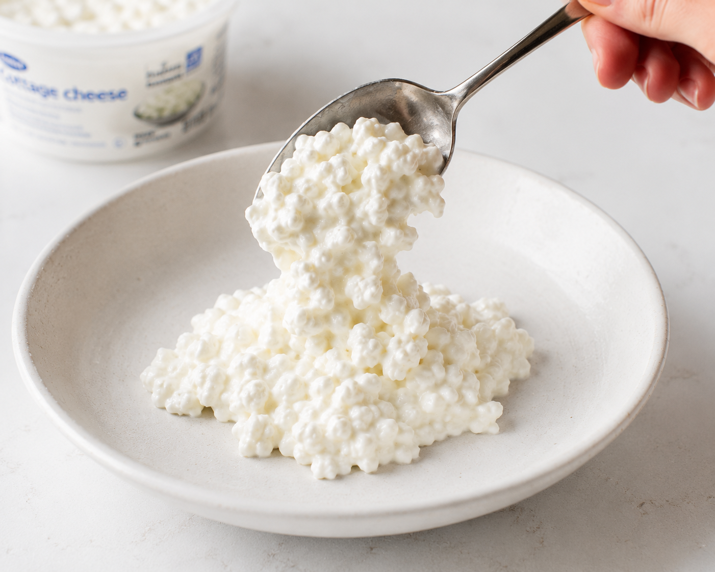 Spooning creamy cottage cheese into a wide shallow bowl