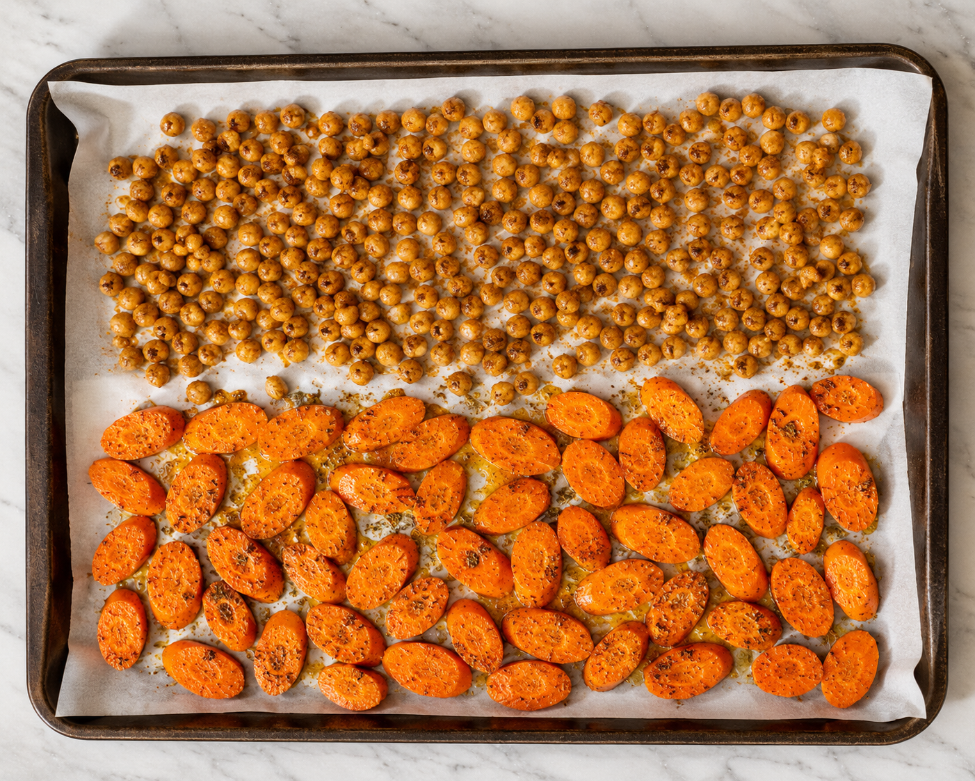 Seasoned carrots and chickpeas arranged on a baking sheet ready to roast