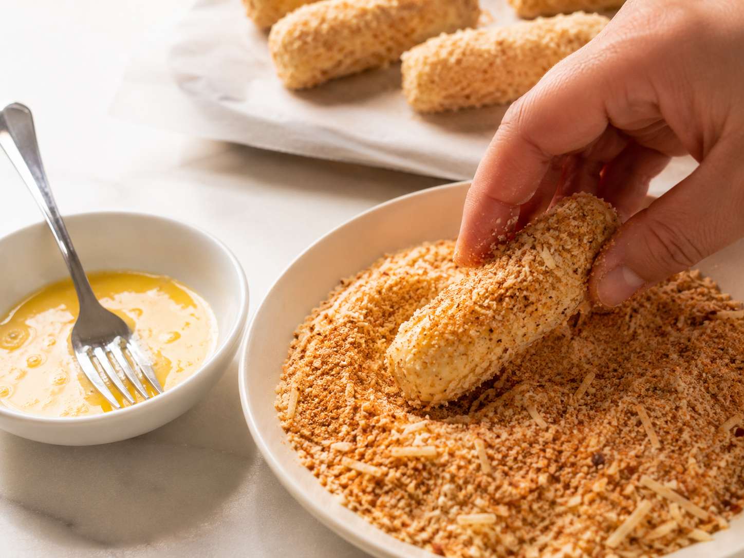 Rolling cauliflower mozzarella sticks in panko and parmesan coating after egg wash