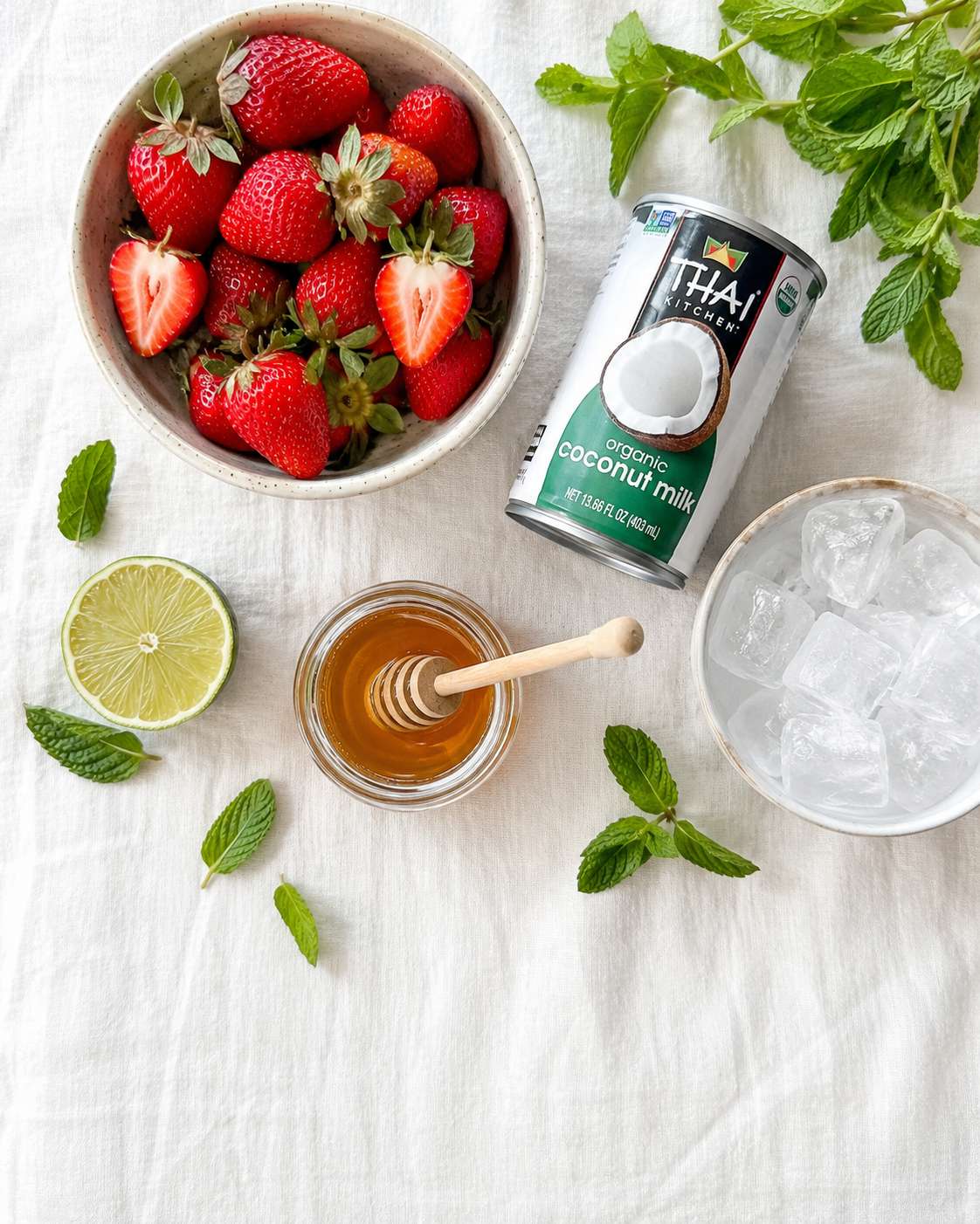 All strawberry coconut refresher ingredients laid out — fresh strawberries, coconut milk, lime, honey, sparkling water and mint