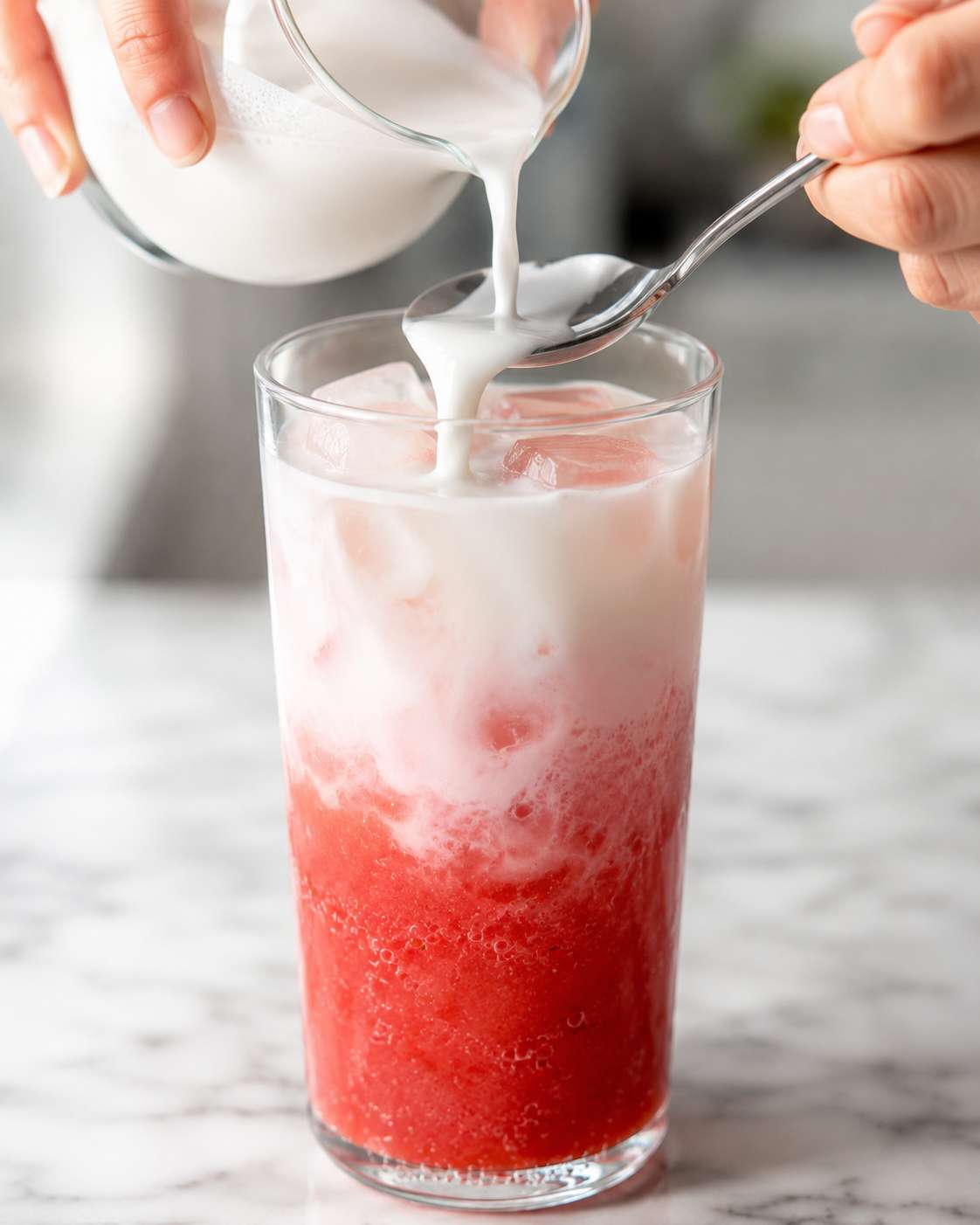 Gently pouring coconut milk over the back of a spoon onto the strawberry layer — creating a beautiful gradient
