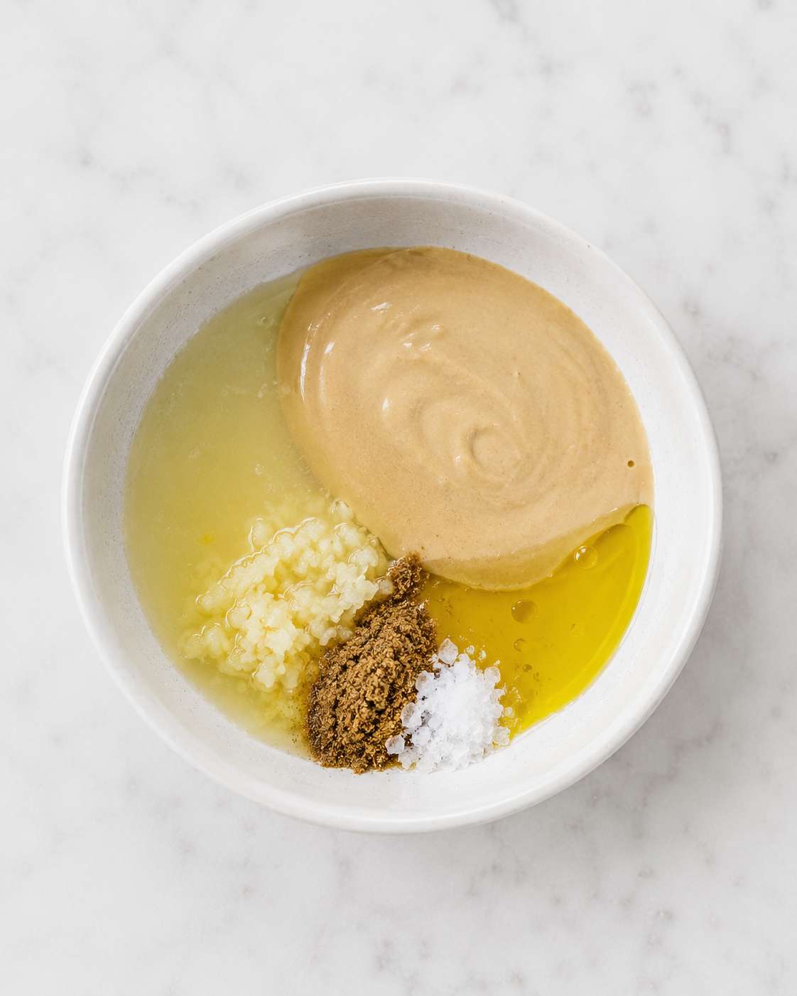 Tahini, lemon juice, garlic, olive oil and spices added to a small bowl — ready to whisk together