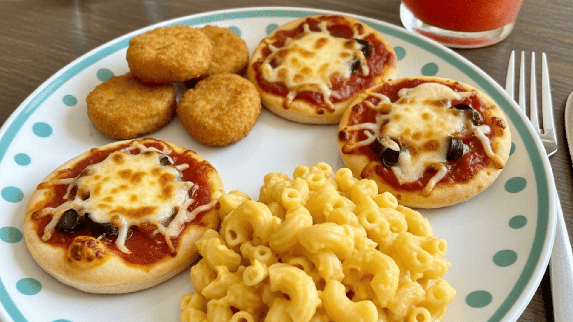 Homemade baked chicken nuggets, mini pizza, and mac and cheese arranged on a kid's plate, bright natural light