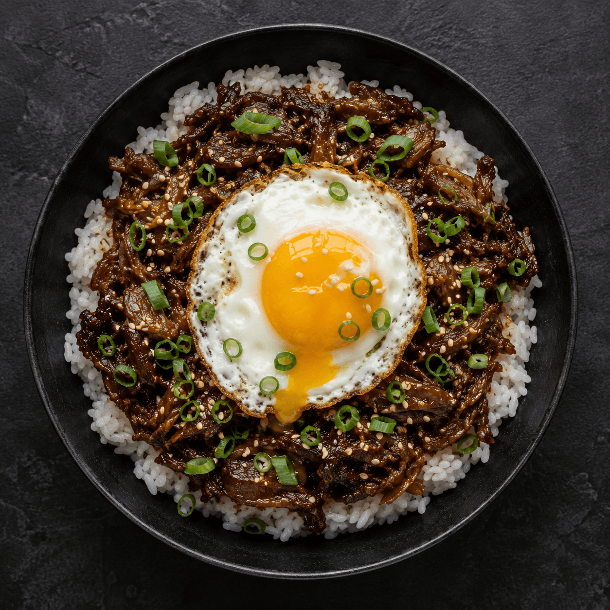 Korean-style beef bulgogi bowl over rice with sesame seeds, scallions, and a fried egg