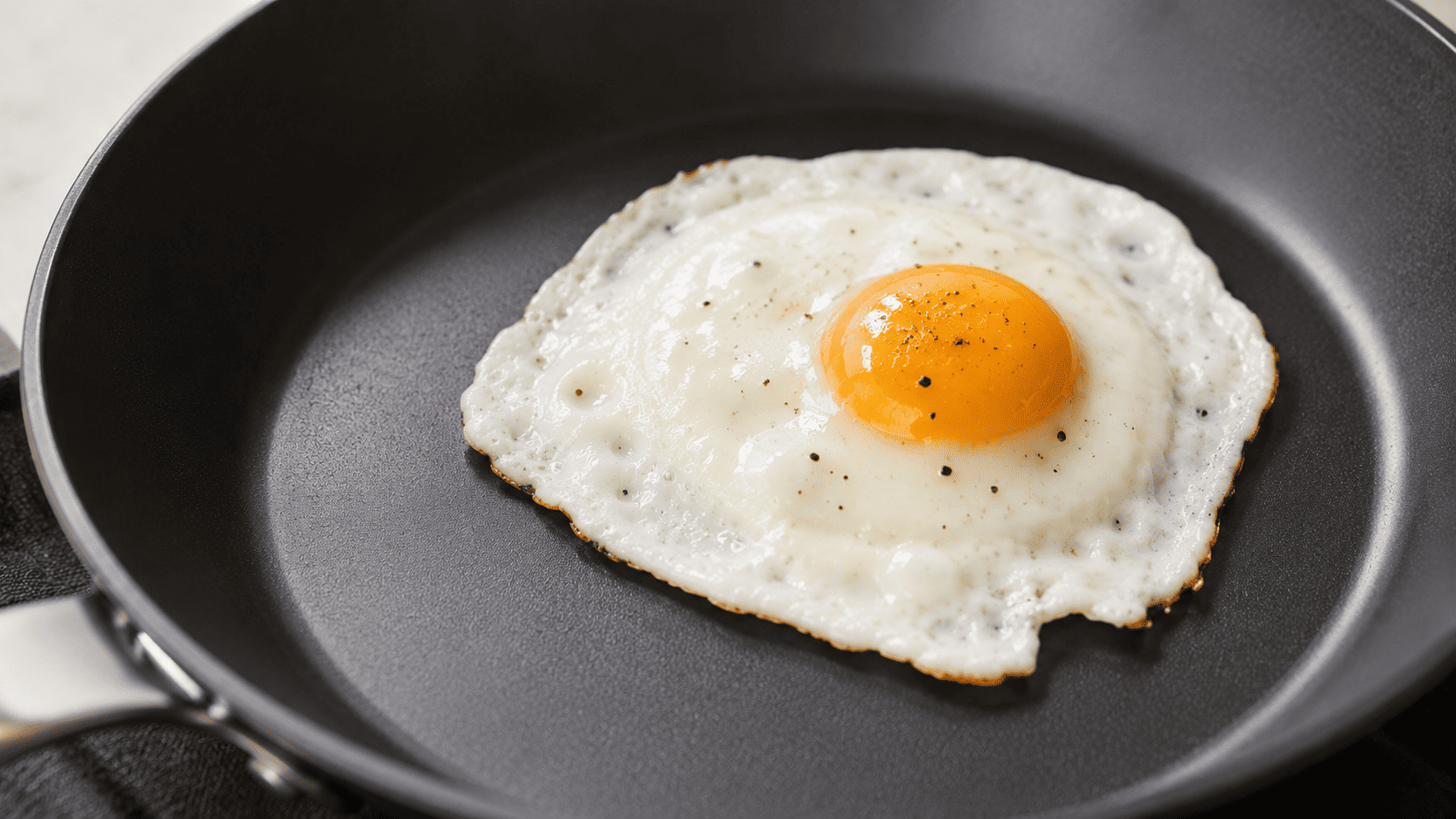 Close-up of a dark ceramic-coated non-stick pan with a single fried egg releasing cleanly, minimal styling