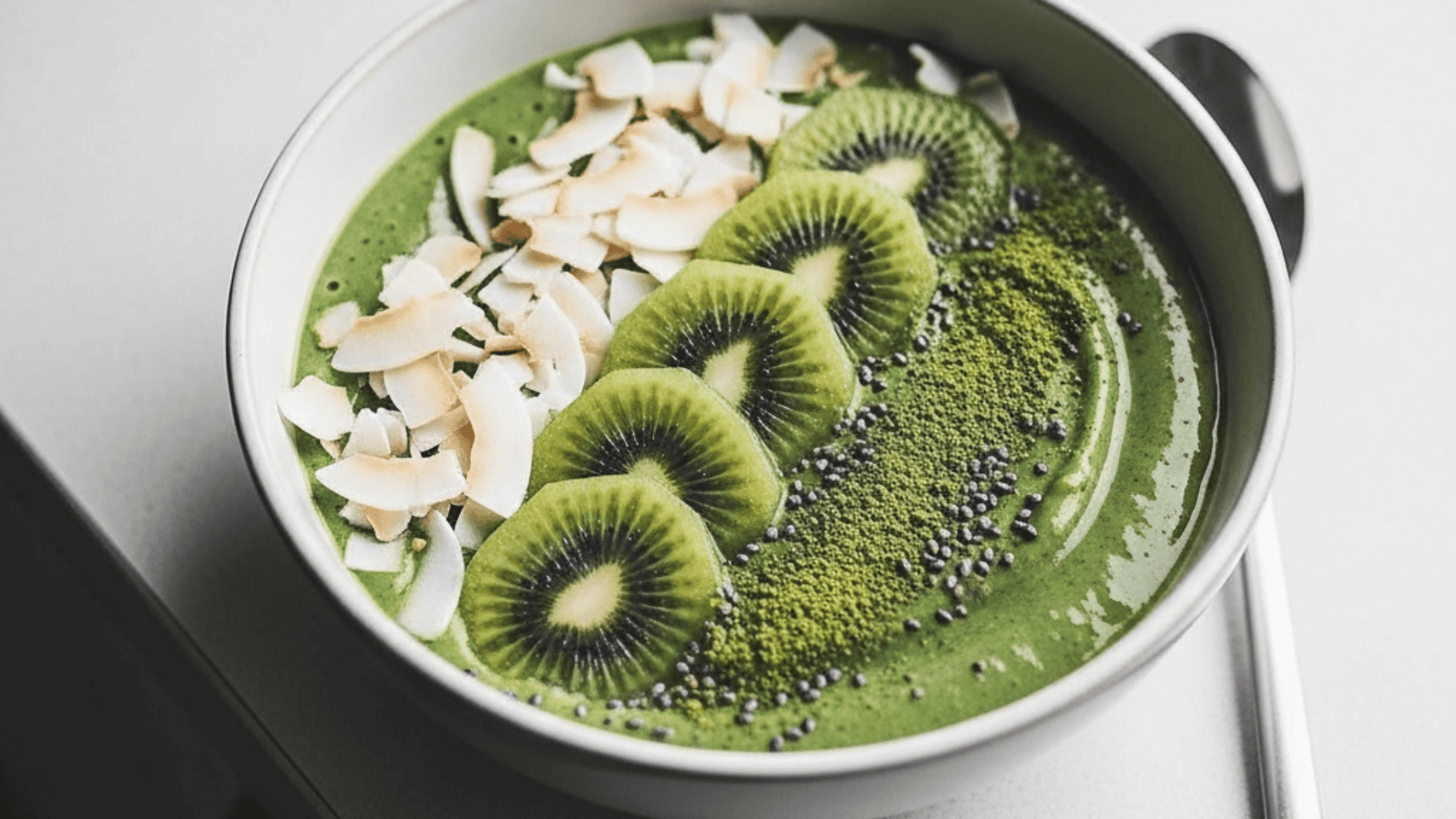 Earthy matcha-green coconut smoothie bowl with coconut flakes, kiwi and a matcha dusting