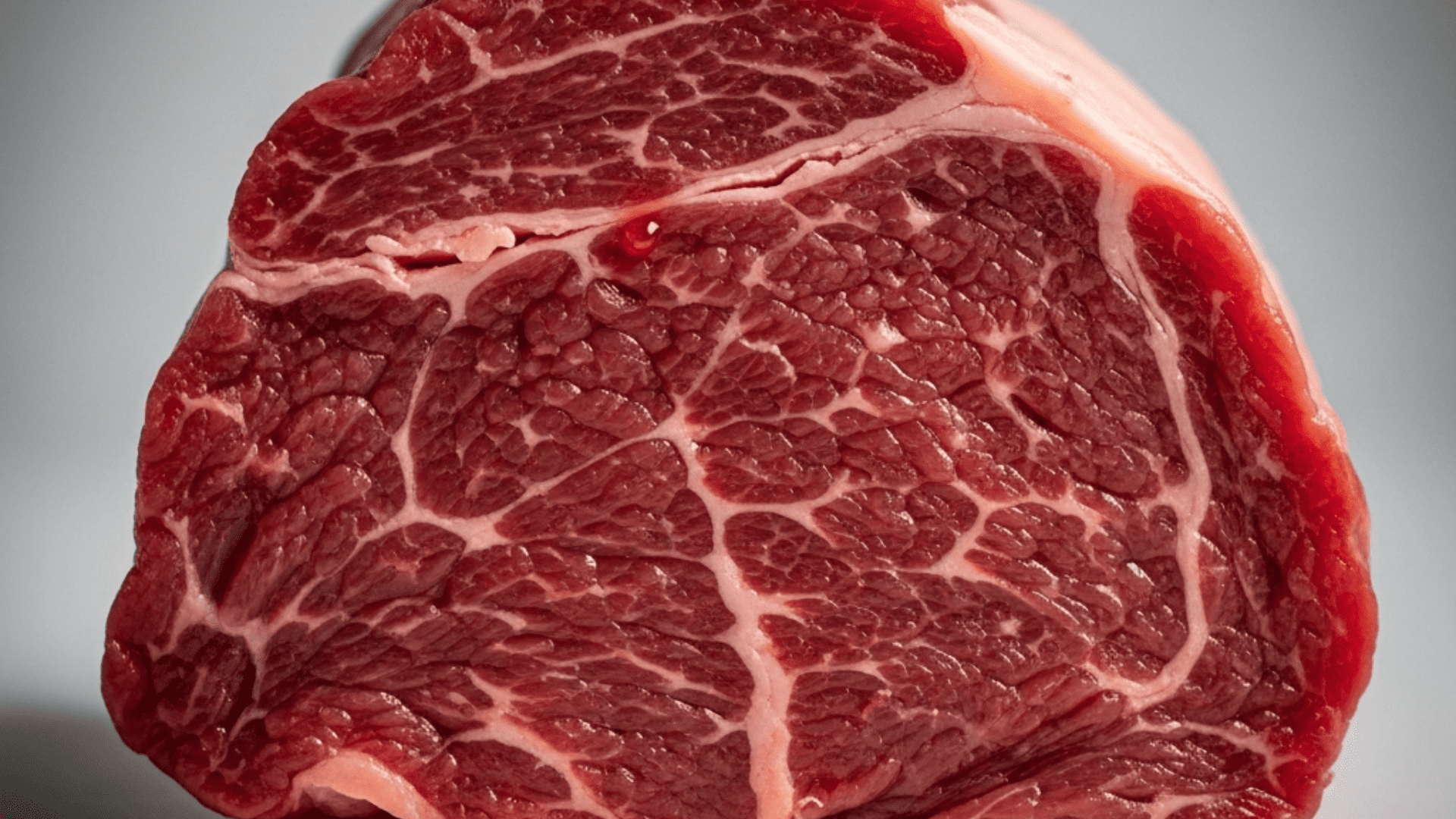 Extreme close-up of raw beef showing the grain of the muscle fibers, deep red, a few droplets of myoglobin-rich liquid, moody studio light
