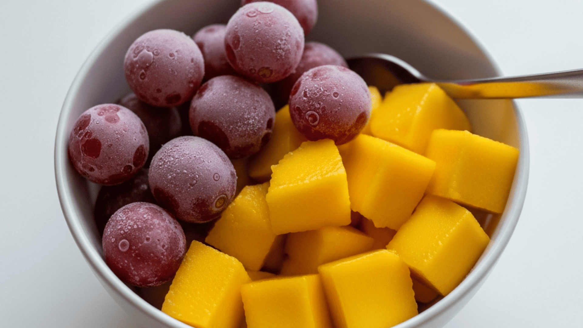 Frozen grapes and mango chunks in a small bowl, bright natural light