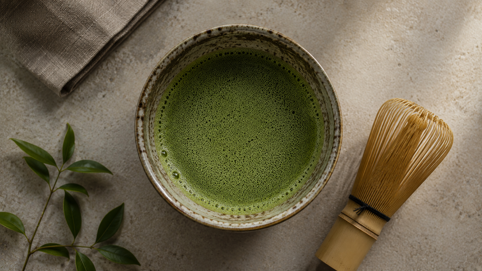 Overhead flat-lay of whisked matcha in a chawan with fine foam, bamboo chasen resting beside it, soft natural window light
