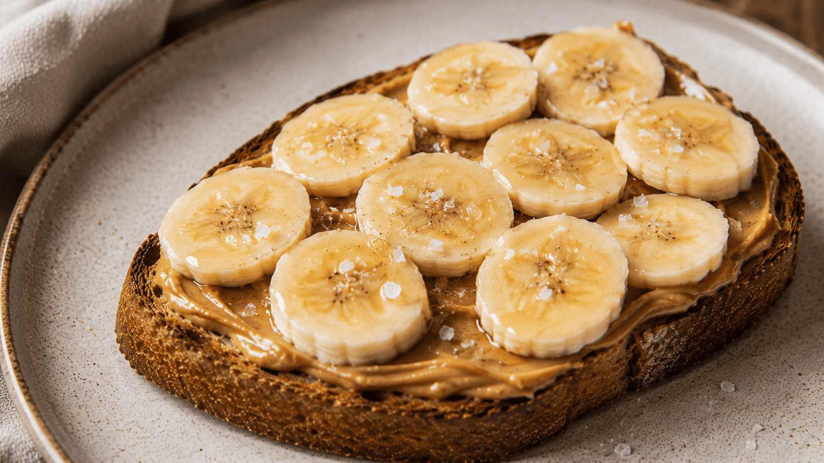 Peanut butter toast with banana slices and a pinch of visible flaky salt