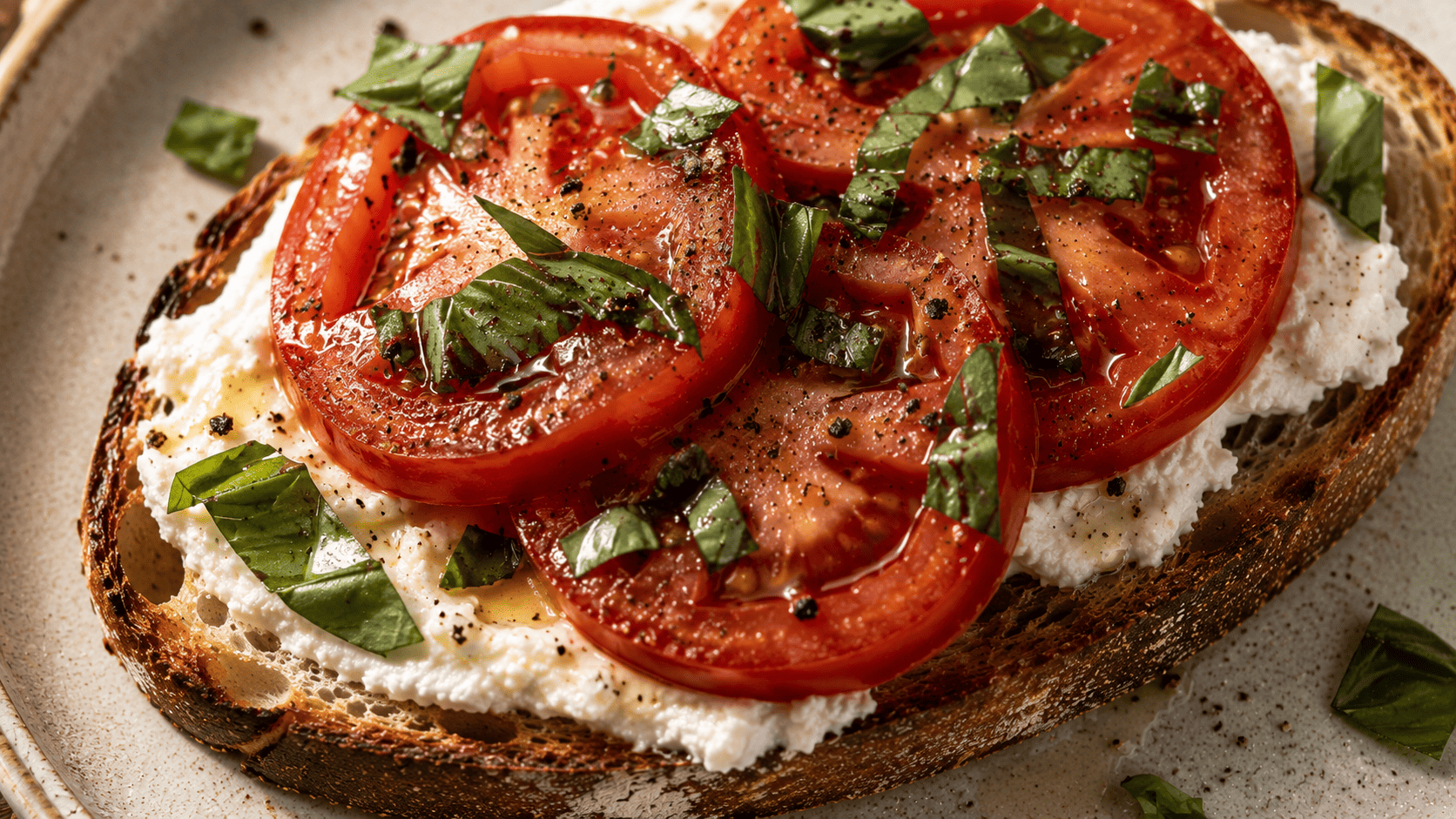 Ricotta toast with thick tomato slices and torn basil, olive oil sheen