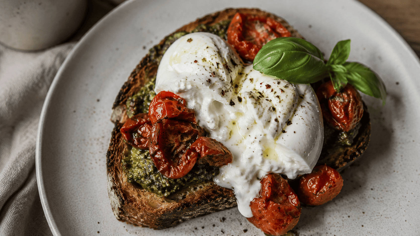 Torn burrata over pesto toast with collapsed roasted cherry tomatoes