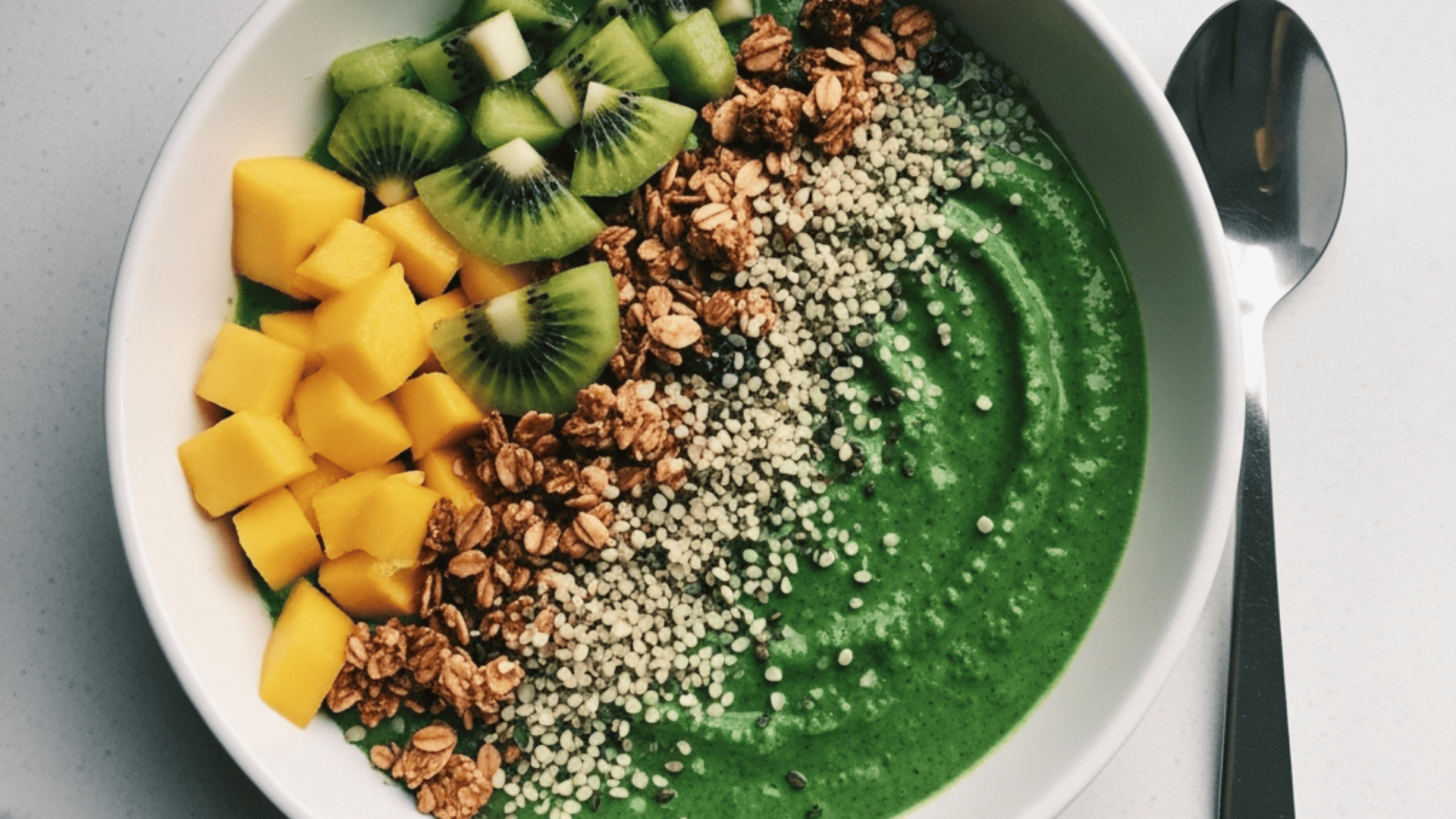 Vivid green spinach-mango bowl topped with kiwi, granola and hemp seeds
