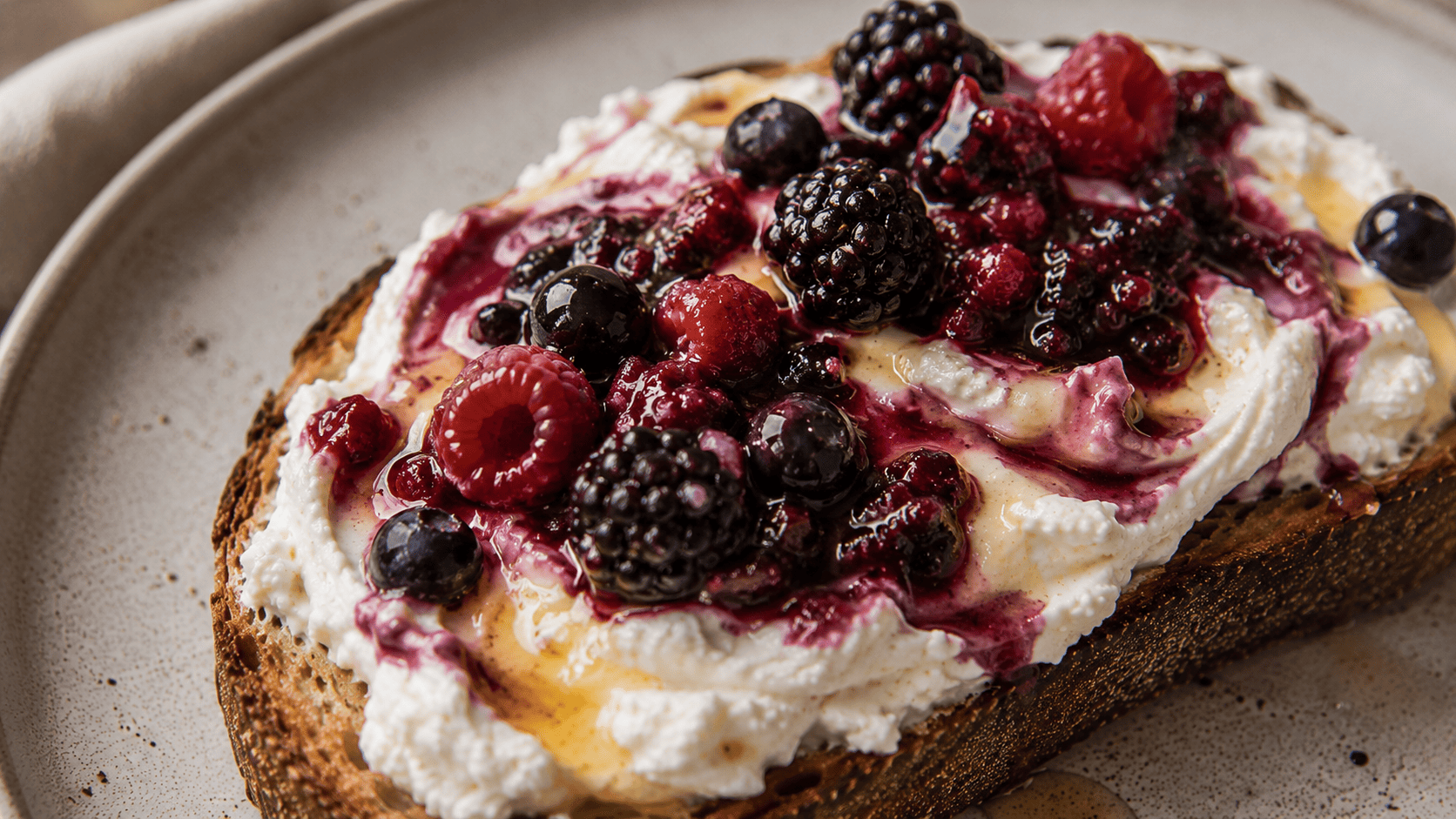 Whipped ricotta toast swirled with berries and honey, close-up texture shot, soft window light