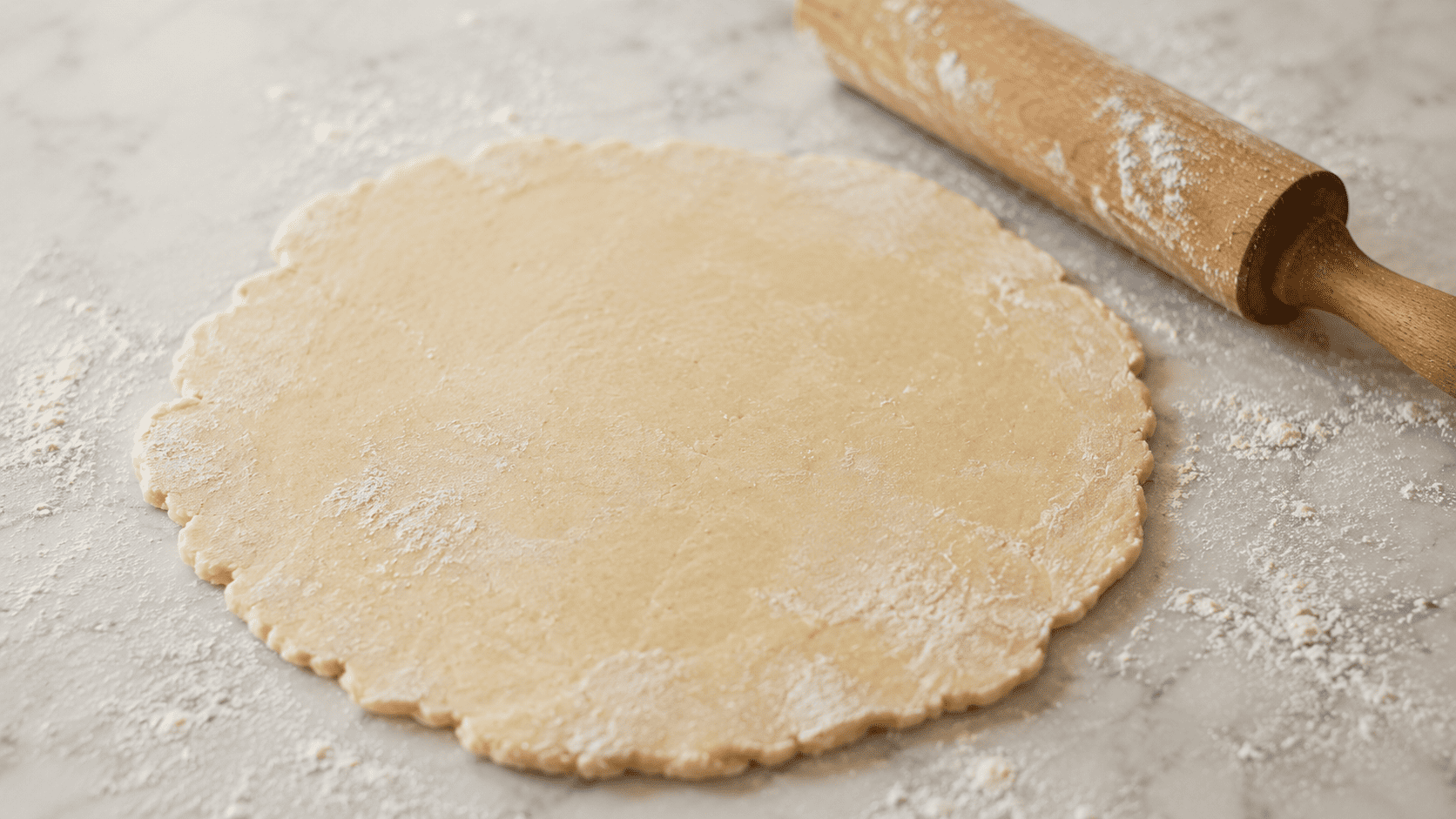 A rough circle of pale pastry dough rolled out on a lightly floured white marble counter, ready to be filled