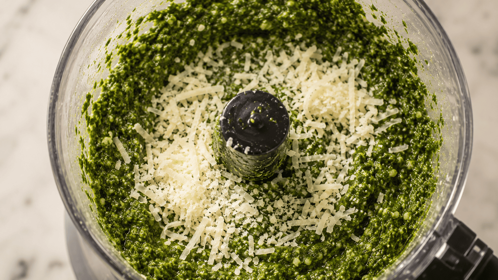 Grated Parmesan cheese being pulsed into the basil pesto