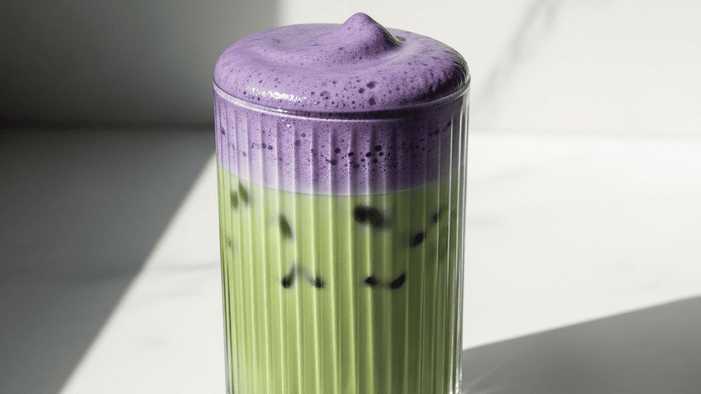 Deep purple-blue foam settling over green matcha in a tall glass