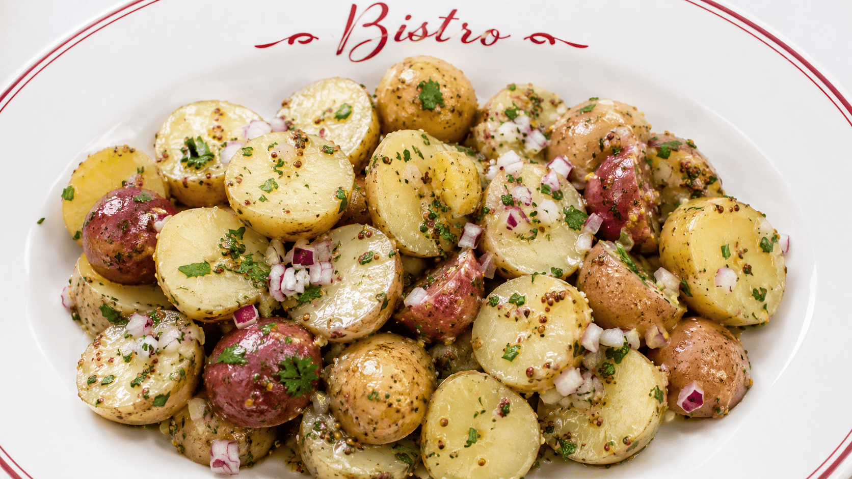 Warm fingerling potatoes glossy with Dijon vinaigrette, shallots and parsley scattered on top, rustic wooden bowl