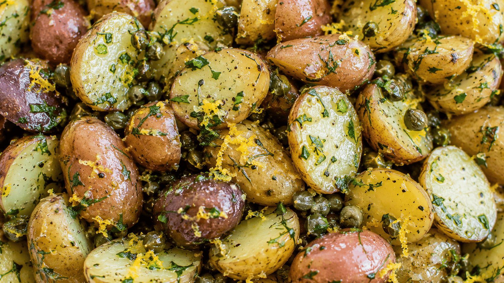 Halved fingerling potatoes tossed with lemon zest, capers, and fresh herbs, close-up texture shot