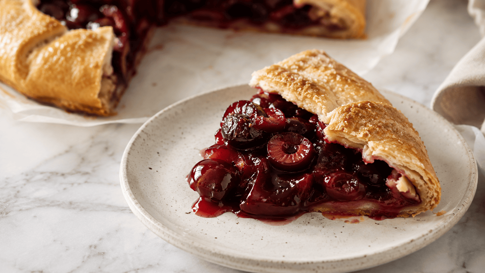 Sliced cherry galette ready to serve, wedges cut on a wooden board showing the golden crust and jammy cherry filling