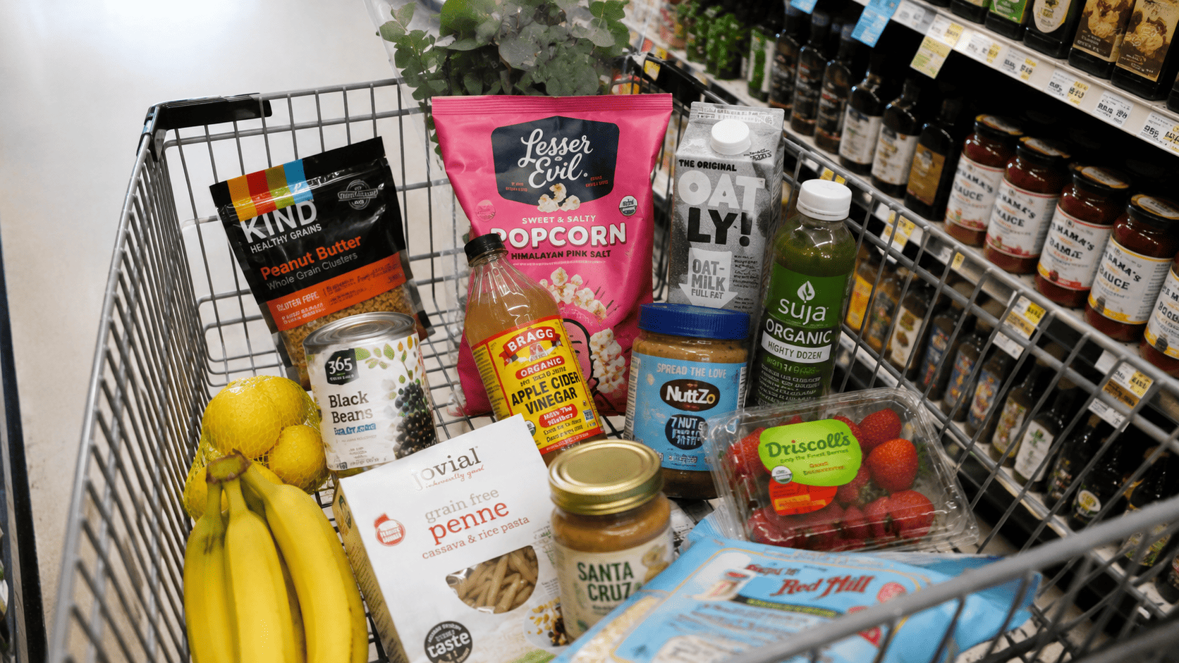 A shopping cart with a few colorful, trendy grocery items mixed among basics