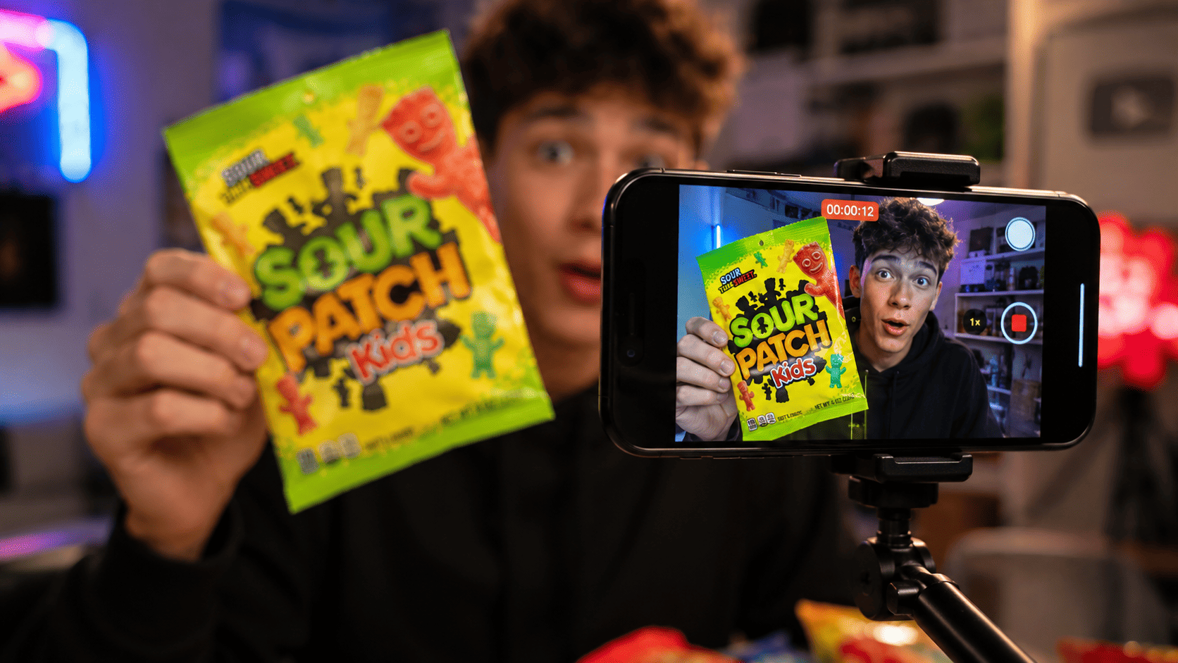 A smartphone filming a brightly colored American snack held up to camera, shallow depth of field, reaction-video framing