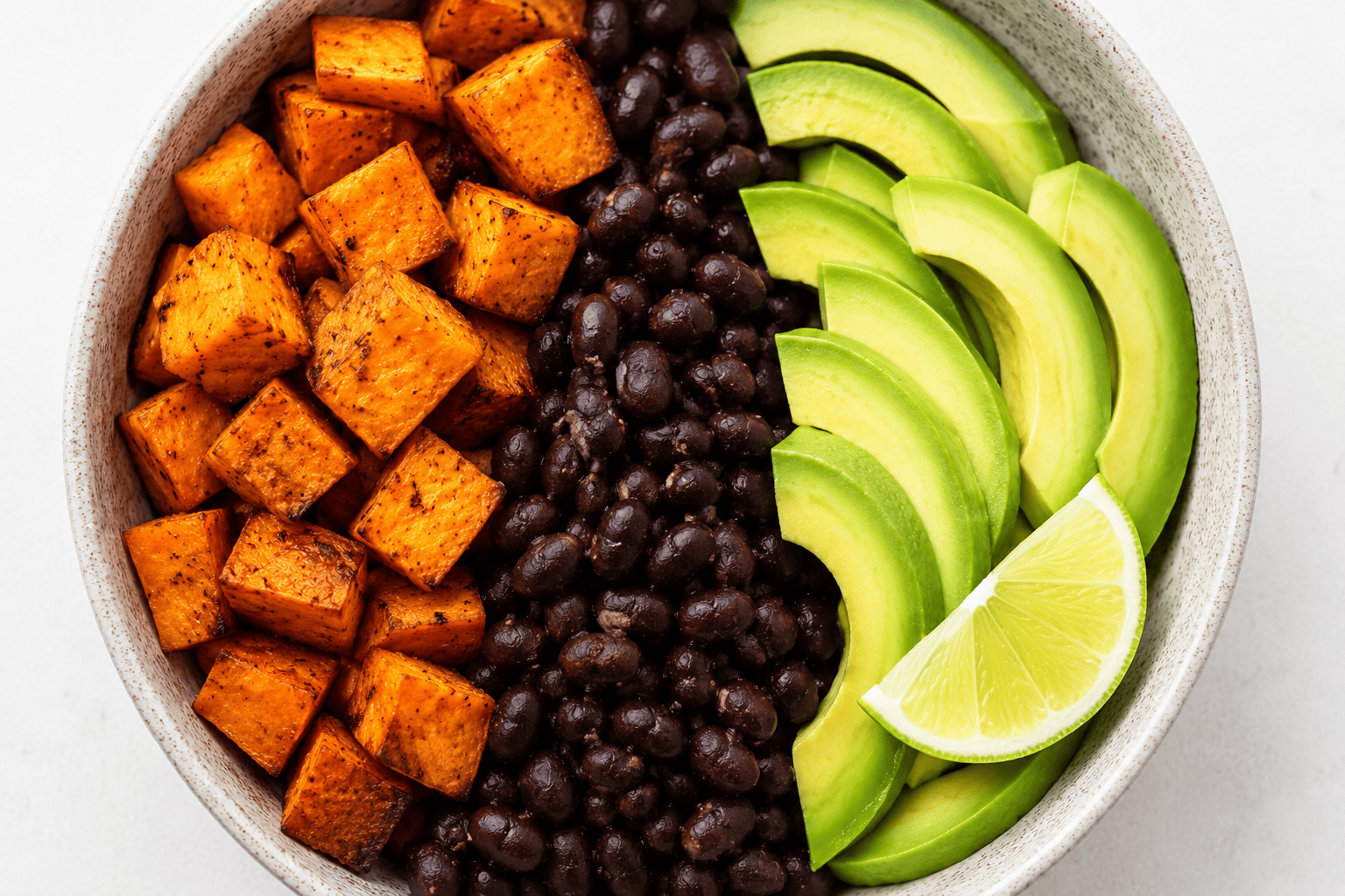 Colorful sweet potato and black bean bowl with sliced avocado and lime wedge, overhead shot