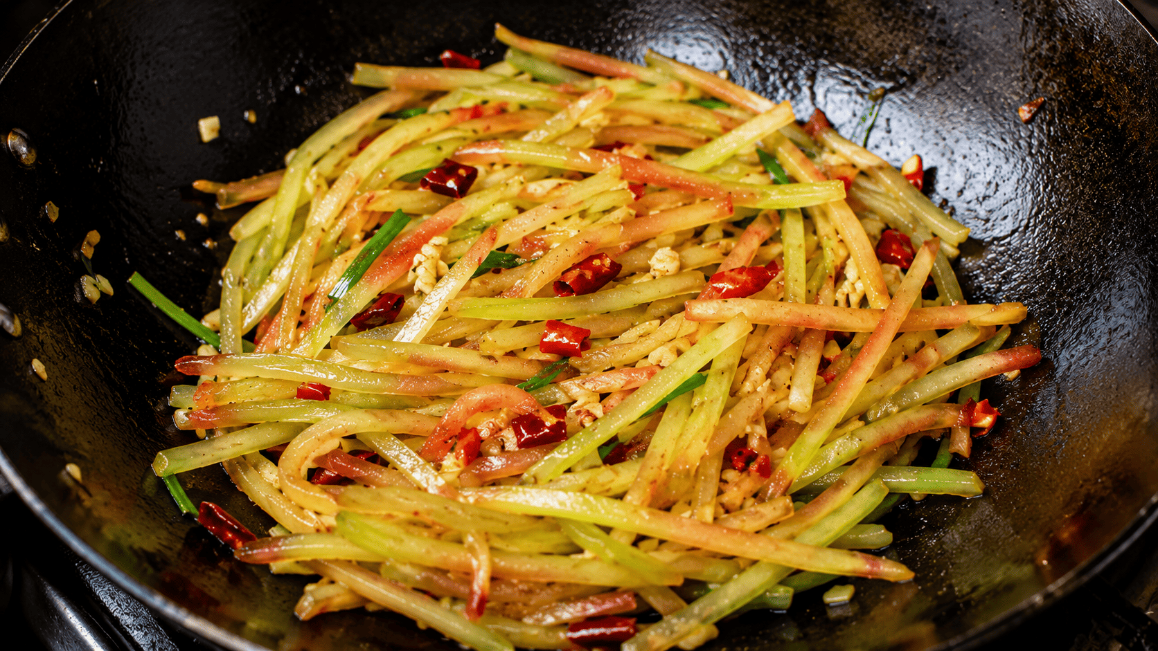 Julienned watermelon rind stir-fried with garlic and chili in a dark wok