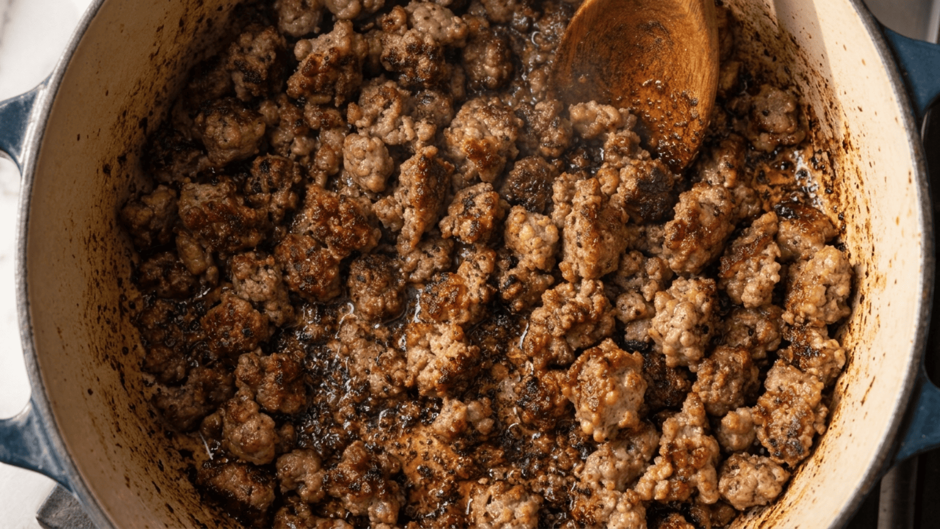 Crumbled Italian sausage browning in a Dutch oven with a wooden spoon