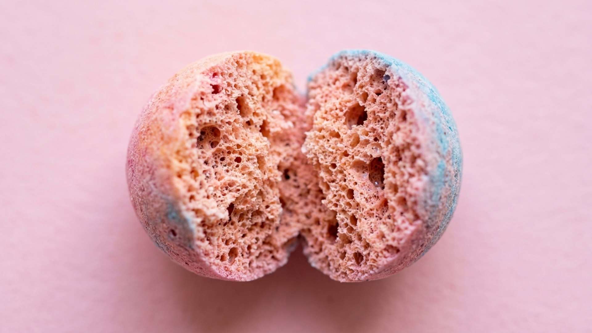 Macro close-up of a split freeze-dried candy showing its porous foam-like interior on a pastel backdrop